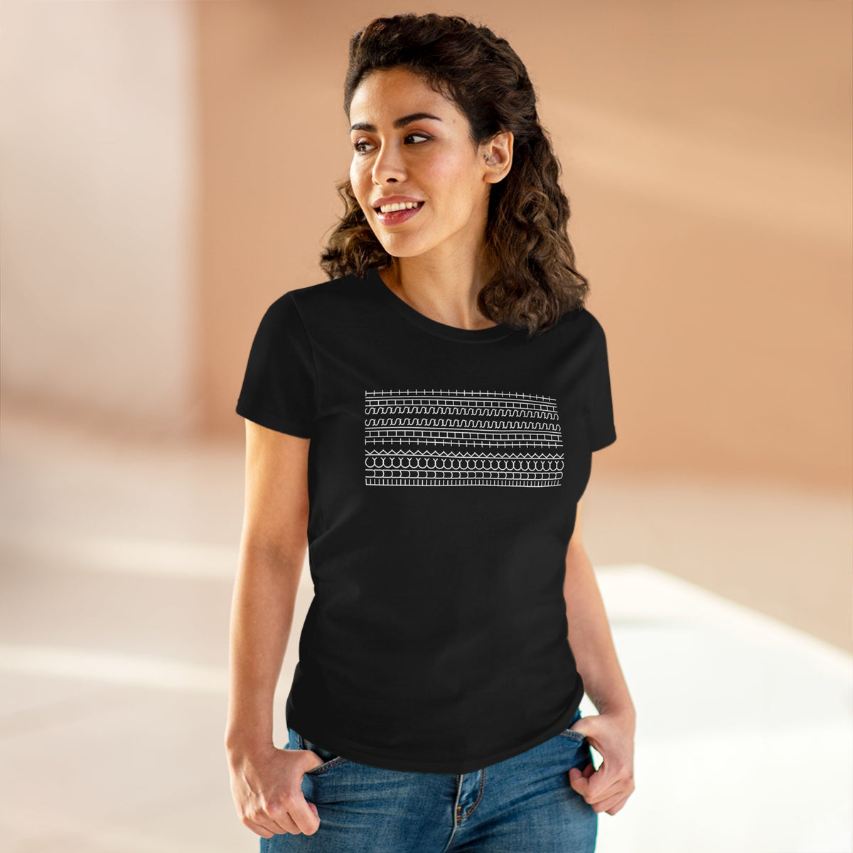 A woman wearing a black short-sleeve crewneck t-shirt with a white geometric patterned chest graphic, paired with blue jeans, set against a warm beige background.
