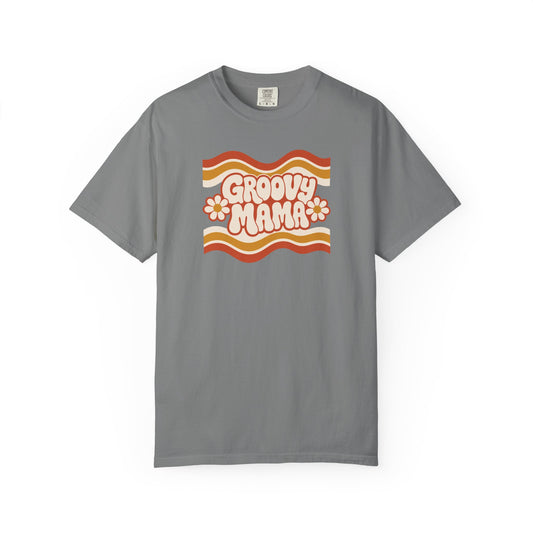 A gray short-sleeve crewneck t-shirt featuring a retro 1970s-style graphic on the chest with wavy orange, yellow, and white stripes, the text 'Groovy Mama' in pink bubble letters, and two pink-and-white daisies.