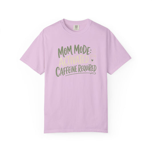 A light purple short-sleeve crewneck t-shirt with a graphic text print reading 'MOM MODE ACTIVATED CAFFEINE REQUIRED' in olive green and pale yellow, displayed on a clean white background.