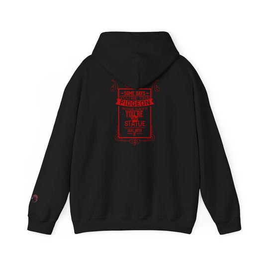 Black hoodie with a red graphic print on the back featuring the text 'SOME DAYS YOU'RE THE PIDGEON SOME DAYS YOU'RE THE STATUE DEAL WITH IT' in a vintage-style border design.