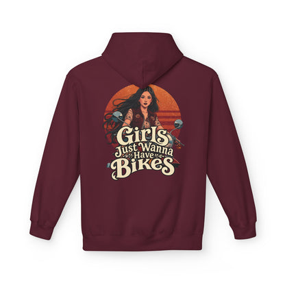 A maroon pullover hoodie shown from the back, featuring a large graphic print of a woman with long dark hair in front of a retro orange sunset. The text 'Girls Just Wanna Have Bikes' is written in a vintage cream-colored font.