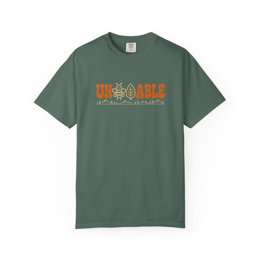 A green crewneck t-shirt with a graphic on the chest reading 'UNBEELEAFABLE' in orange, featuring a bee and a mountain graphic, displayed on a clean white background.