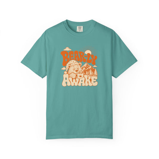 A teal short-sleeve crewneck t-shirt with a retro-style graphic on the chest reading 'BEARLY AWAKE' in orange and cream, featuring a bear and mountain illustration, shown on a plain white background.