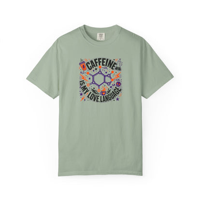 A sage green short-sleeve t-shirt with a colorful graphic on the chest that reads 'CAFFEINE IS MY LOVE LANGUAGE' around a chemical structure, displayed on a clean white background.