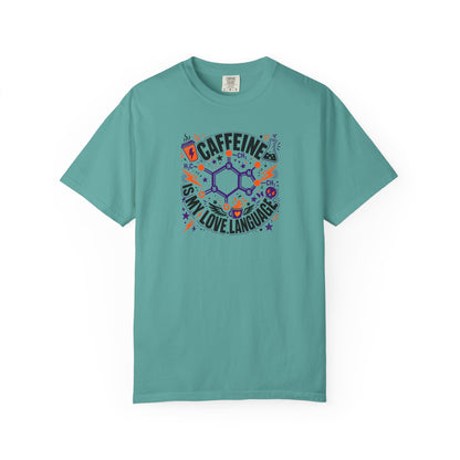 A sea blue short-sleeve crewneck t-shirt featuring a colorful graphic print on the front. The graphic displays a chemical structure surrounded by the text 'CAFFEINE IS MY LOVE LANGUAGE' in black, accented with purple, orange, and blue doodles.