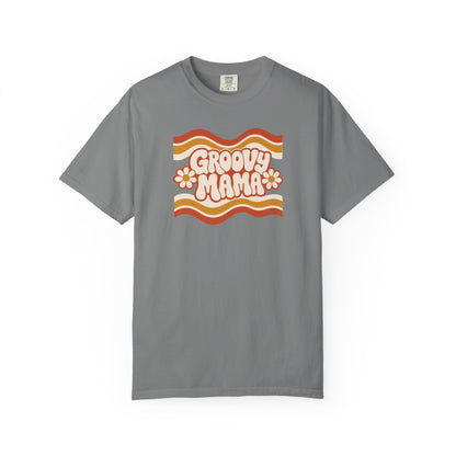 A gray short-sleeve crewneck t-shirt featuring a retro 1970s-style graphic on the chest with wavy orange, yellow, and white stripes, the text 'Groovy Mama' in pink bubble letters, and two pink-and-white daisies.