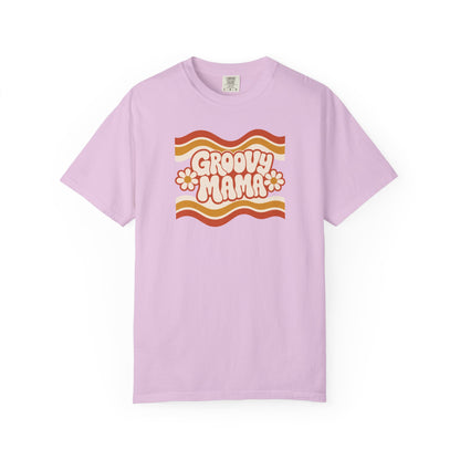 A light purple short-sleeve t-shirt with a retro 1970s-style graphic on the chest reading 'Groovy Mama' in cream with orange and yellow wavy stripes and flower details, displayed on a clean white background.