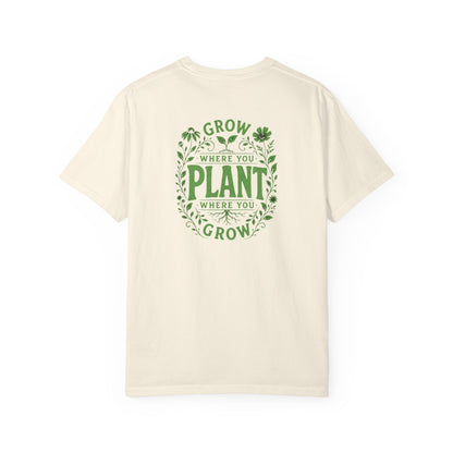 An ivory short-sleeve t-shirt with a green graphic on the back reading 'GROW WHERE YOU PLANT WHERE YOU GROW' surrounded by leaves and clovers, shown against a plain white background.