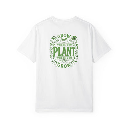 A white short-sleeve crewneck t-shirt featuring a green circular graphic on the back with the text 'GROW WHERE YOU PLANT WHERE YOU GROW' surrounded by leaf and clover illustrations.