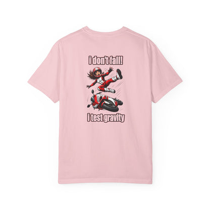 A light pink short-sleeve t-shirt with a graphic print on the front. The graphic features an anime-style character falling off a red and black motorcycle, with the text 'I don't fall!' above and 'I test gravity' below.