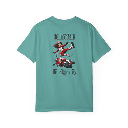A teal short-sleeve t-shirt with a graphic print on the back showing a cartoon girl falling off a motorcycle with the text 'I don't fall' above and 'I test gravity' below.
