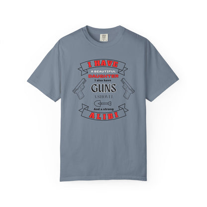 A blue jean short-sleeve crewneck t-shirt with a graphic print on the front. The graphic features the text 'I have a beautiful daughter,i also have guns, a shovel and a strong alibi' in black and red lettering, accompanied by illustrations of two pistols and a shovel.