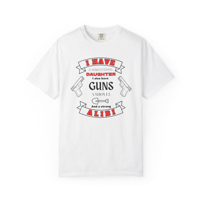 A white short-sleeve crewneck t-shirt with a graphic print on the front. The graphic features the text 'I have a beautiful daughter,i also have guns, a shovel and a strong alibi' in black and red lettering, accompanied by illustrations of two pistols and a shovel.