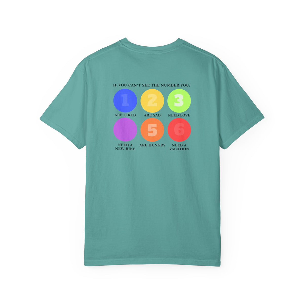 A teal green short-sleeve t-shirt with a colorful graphic on the back. The graphic features six colored circles (blue, yellow, green, purple, orange, red) numbered 1 through 6, with text reading 'IF YOU CAN'T SEE THE NUMBER, YOU: 1 Are Tired 2 Are sad 3 Need Love 4 Need a new bike 5 Are hungry 6 Need a vacation'