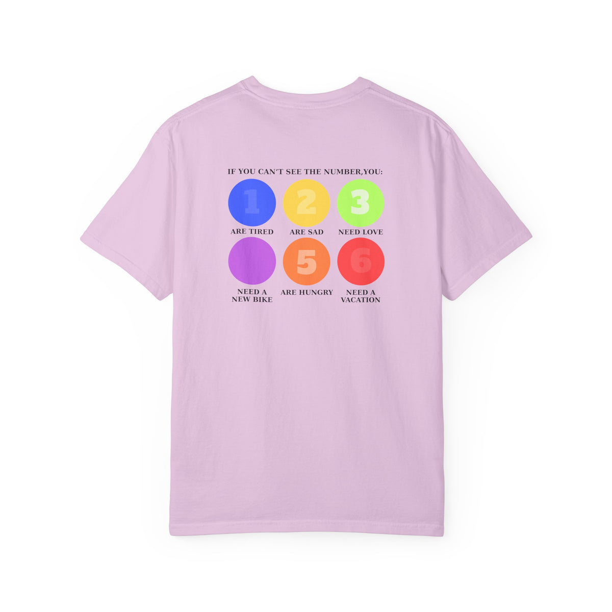 A pink short-sleeve t-shirt with a colorful graphic on the back. The graphic features six colored circles (blue, yellow, green, purple, orange, red) numbered 1 through 6, with text reading 'IF YOU CAN'T SEE THE NUMBER, YOU: 1 Are Tired 2 Are sad 3 Need Love 4 Need a new bike 5 Are hungry 6 Need a vacation'