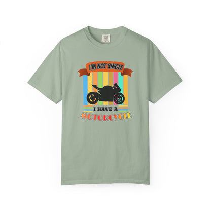 A sage green short-sleeve t-shirt with a colorful graphic on the front featuring a black motorcycle silhouette and the text 'I'M NOT SINGLE I HAVE A MOTORCYCLE' on a white background.