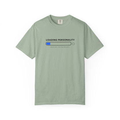 A sage green short-sleeve t-shirt with a graphic on the chest that reads 'LOADING PERSONALITY' above a progress bar with a blue filled segment and the text 'please wait.