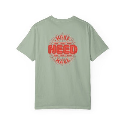 A sage green short-sleeve t-shirt with a red circular graphic on the back that reads 'MAKE THE TIME YOU NEED THE TIME YOU MAKE'.