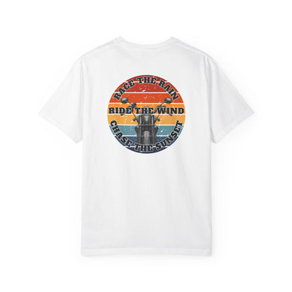 A white short-sleeve crewneck t-shirt with a retro circular graphic on the chest. The graphic features a motorcycle silhouette and the text 'RACE THE RAIN', 'RIDE THE WIND', and 'CHASE THE SUNSET' in a distressed sunset color palette of orange, yellow, and blue.