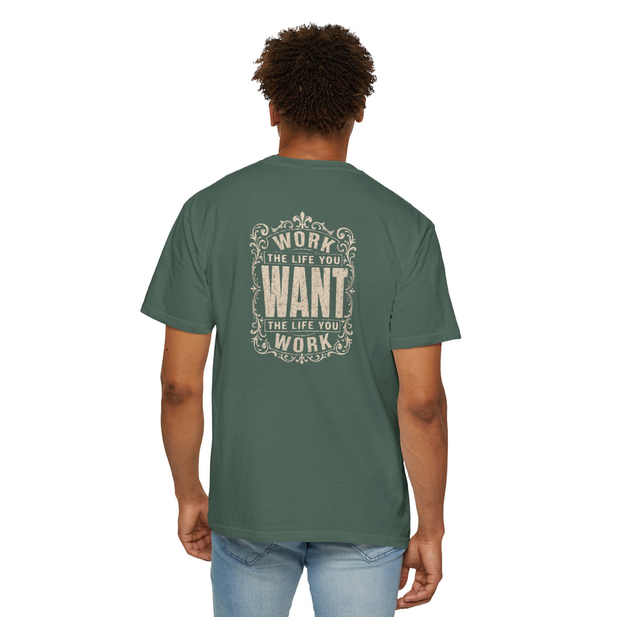 A man wearing a green short-sleeve crewneck t-shirt with a dark white graphic print on the back. The graphic features the motivational quote 'WORK THE LIFE YOU WANT THE LIFE YOU WORK' in a decorative, vintage-style frame.